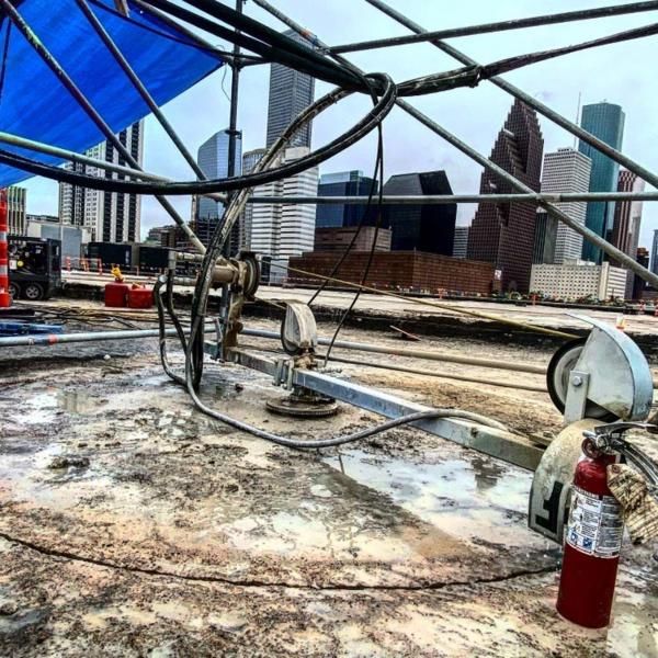 Rooftop construction site with cables, tools, and a fire extinguisher against a city skyline.