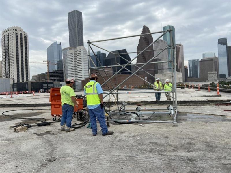 Construction workers in neon vests assembling scaffolding on a rooftop with a city skyline in the background