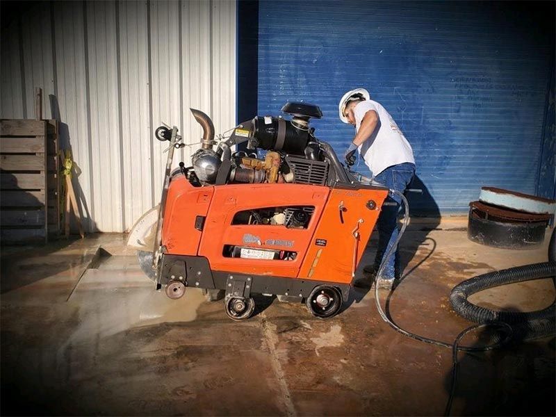 Worker operating an orange floor-cleaning machine in a warehouse-like space