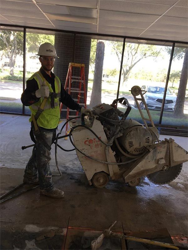 Worker in safety gear standing beside a concrete saw in a covered construction area.