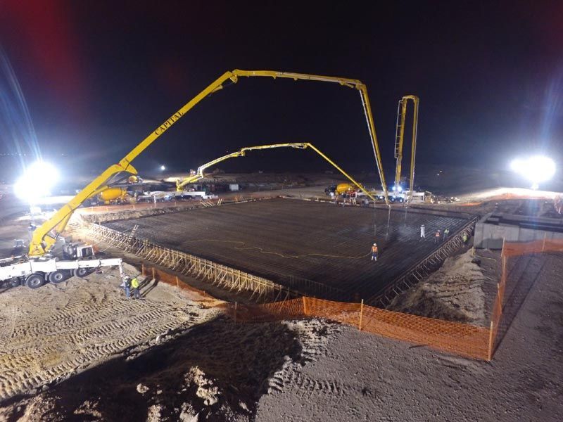 Nighttime construction site with concrete pumps pouring a large foundation slab under bright lights