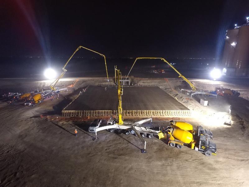 Nighttime construction site with concrete pumps and workers pouring a large foundation slab