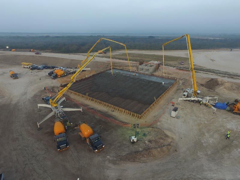 Aerial view of a concrete pour at a large construction site with yellow boom pumps and trucks surrounding a foundation
