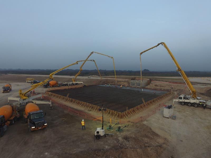 Construction site with concrete pumps pouring a large foundation slab at dusk