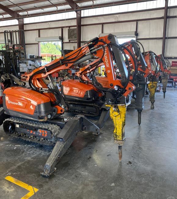 Orange excavators lined up inside a warehouse or equipment garage.