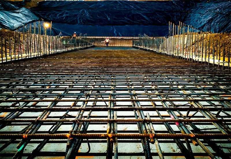 Construction site with steel rebar grid under a lit tunnel at night