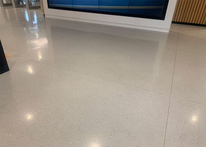 Glossy beige tiled floor in a bright indoor hallway with white wall panels and blue display windows