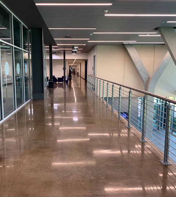 Empty indoor hallway with polished floor, glass wall on left, and railing overlooking a lower level
