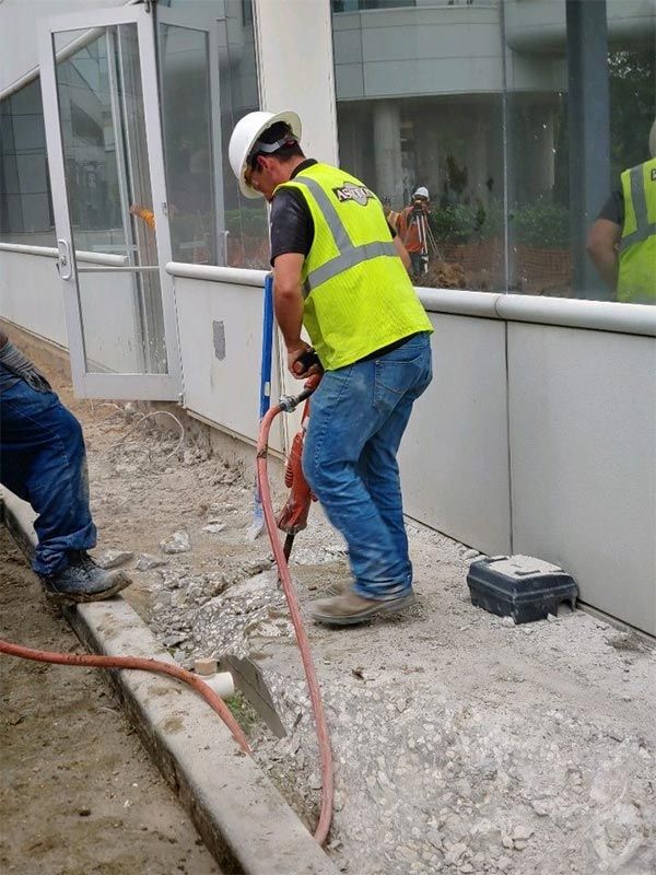 Construction worker in yellow vest using a jackhammer beside a building wall