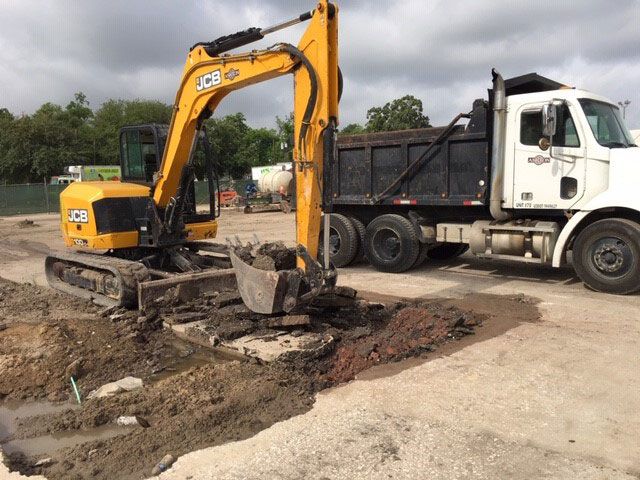 Yellow excavator digging beside a white dump truck at a muddy construction site
