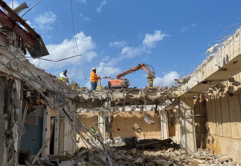 Demolition site with rubble and workers using an excavator under a blue sky