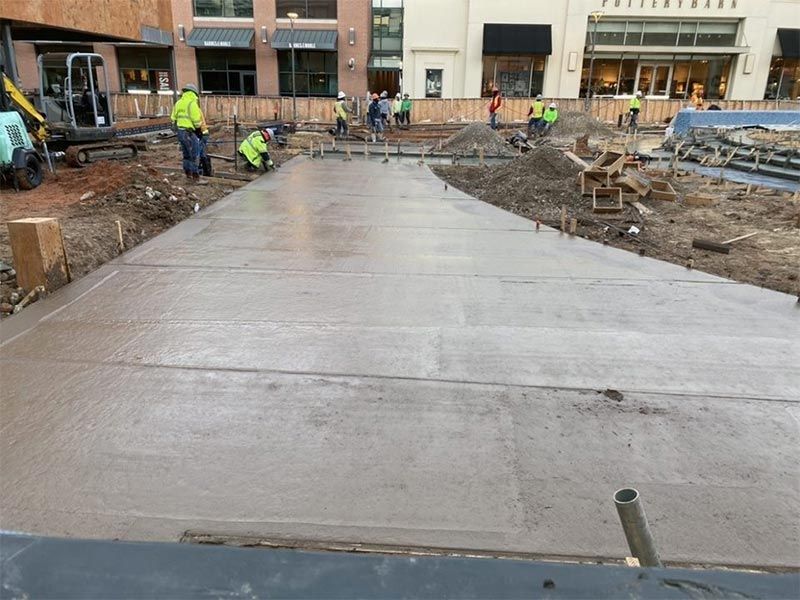 Concrete sidewalk under construction with workers and buildings in the background