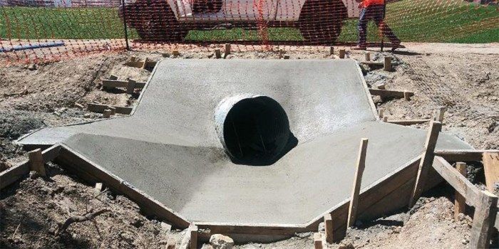 Concrete drainage culvert under construction with a large circular pipe opening and workers in the background