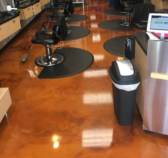 Salon interior with styling chairs, black floor mats, and a trash can on polished orange floor