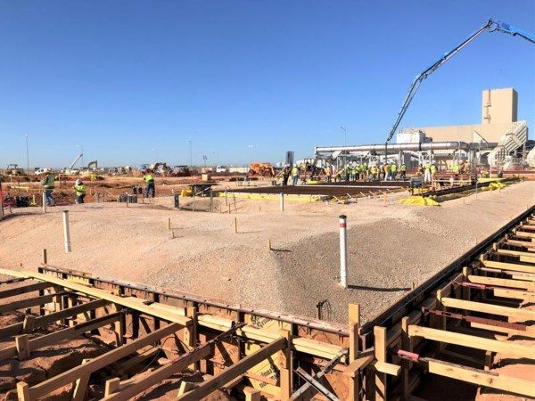 Construction site with concrete foundation, rebar, and workers under a blue sky