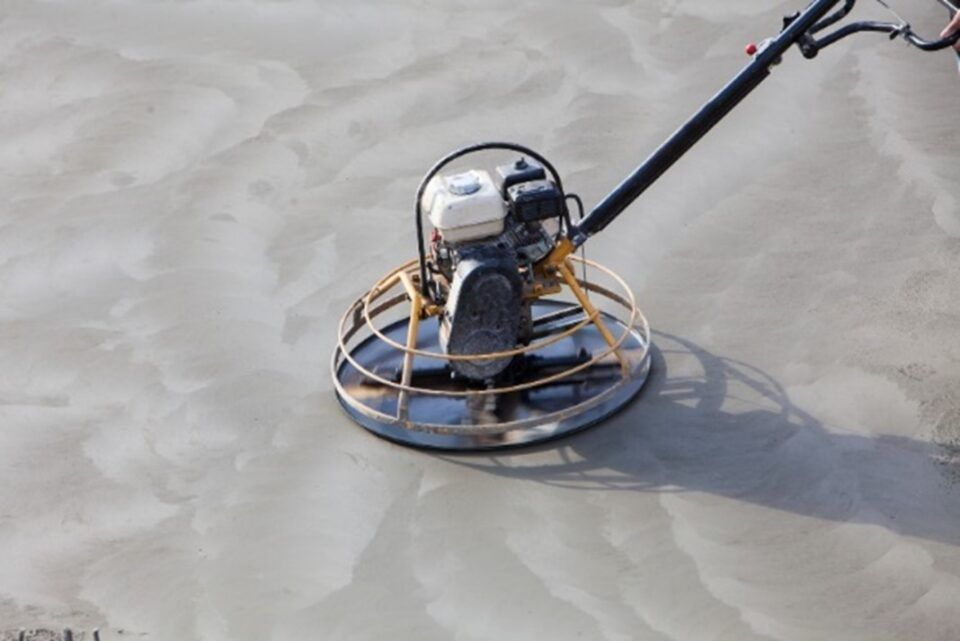 Small metal beach-cleaning device on wet sand, attached to a handle.