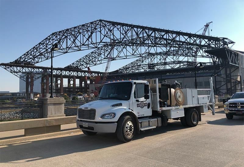 White utility truck parked near a steel truss bridge on a sunny day