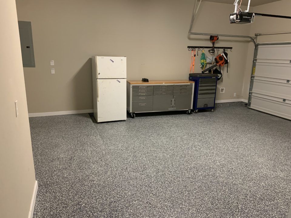 Empty garage with gray carpet, white refrigerator, storage cabinets, and a closed garage door.