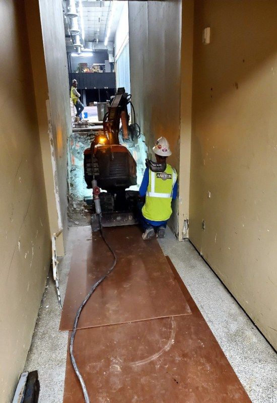 Worker in high-visibility vest and hard hat operating a machine in a narrow hallway construction area