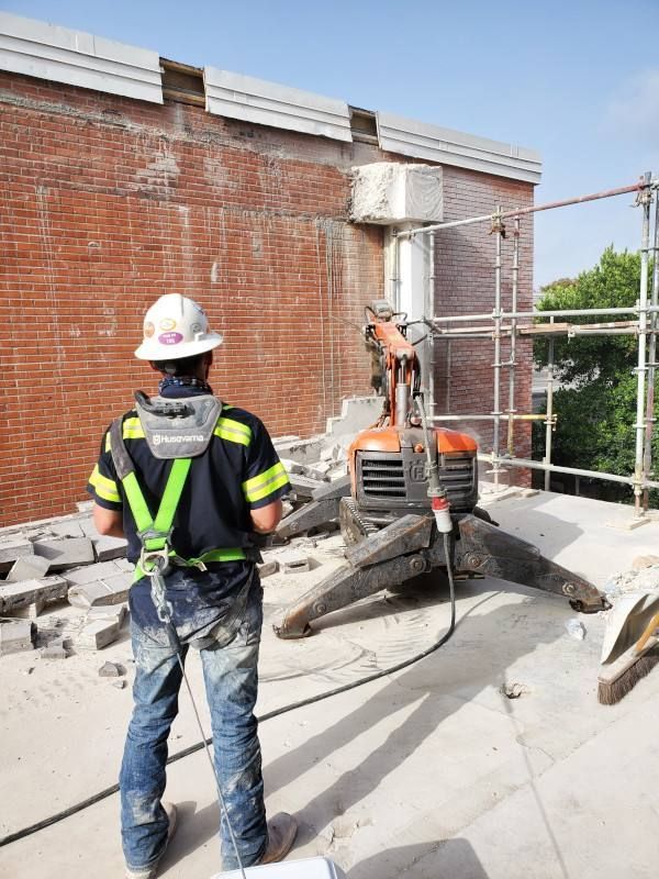 Worker in safety gear operating a small excavator beside a brick wall on a rooftop construction site