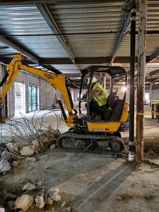 Small excavator clearing concrete debris inside a partially demolished building.