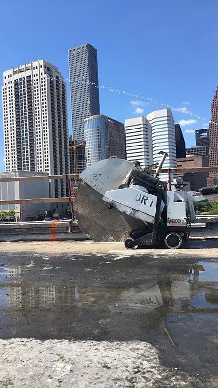 Dump truck tipping gravel at a muddy urban construction site with city skyscrapers in the background