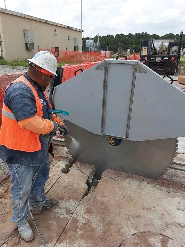 Construction worker in orange vest operating a saw on a large metal cover outdoors