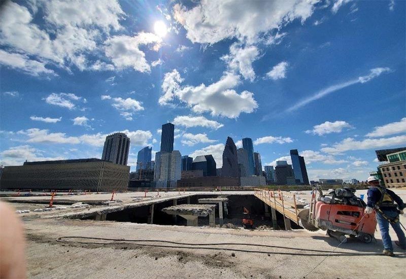 Construction site with excavated ground and a city skyline under a blue, cloudy sky