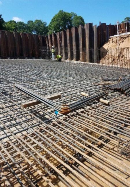Steel rebar foundation grid at a construction site, with workers and retaining walls in the background