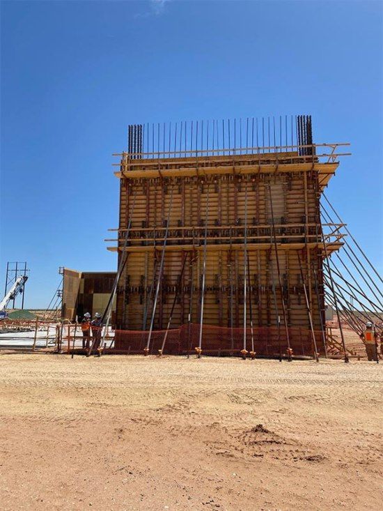 Large concrete formwork structure on a sandy construction site under a clear blue sky.