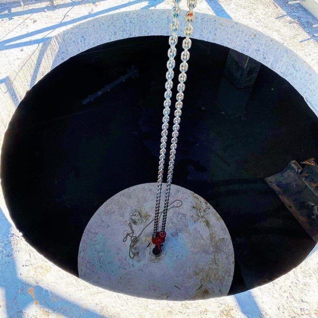 Chain suspending a small red bucket over a large dark circular well opening