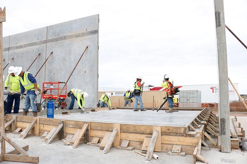 Construction workers pour concrete on a large slab at an outdoor building site.