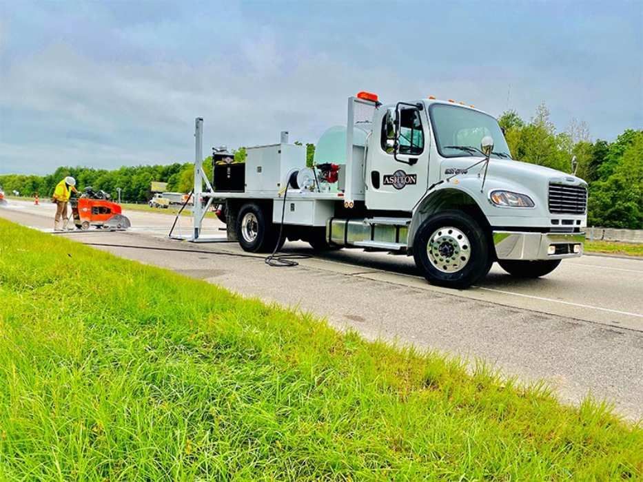 Roadwork crew with orange cones and white utility truck on a roadside under clear skies