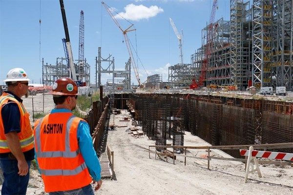 Construction workers in orange vests at a steel-reinforced building site under construction