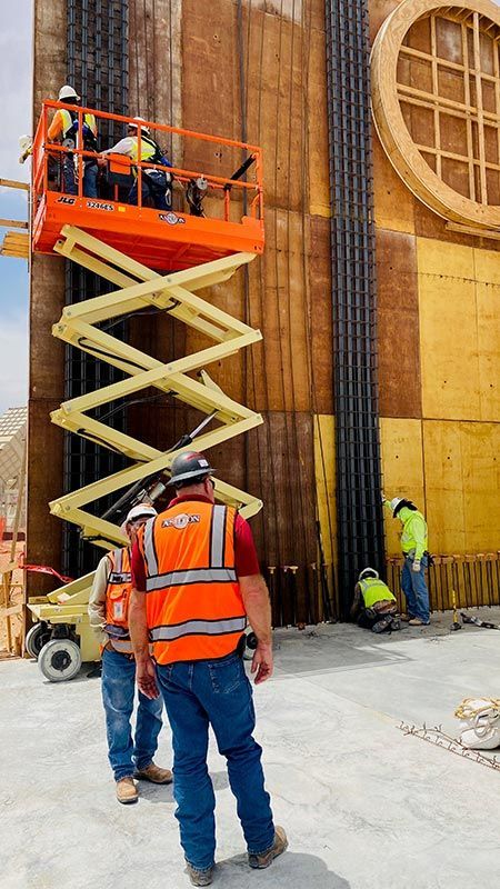 Workers on scissor lift and ground crew installing panels on a tall wooden wall indoors