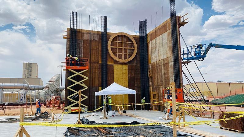 Industrial construction site with a tall wooden structure, workers, scaffolding, and a blue boom lift.