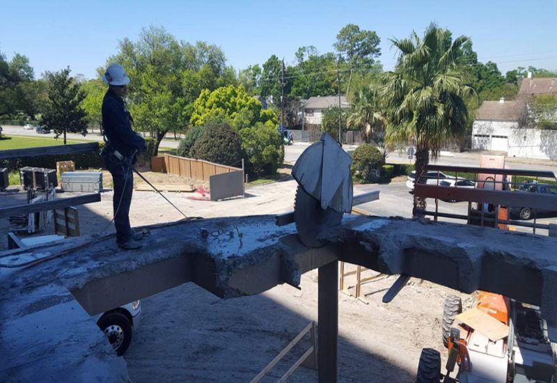 Roofer standing on a rooftop, inspecting a large vent with trees and houses in the background