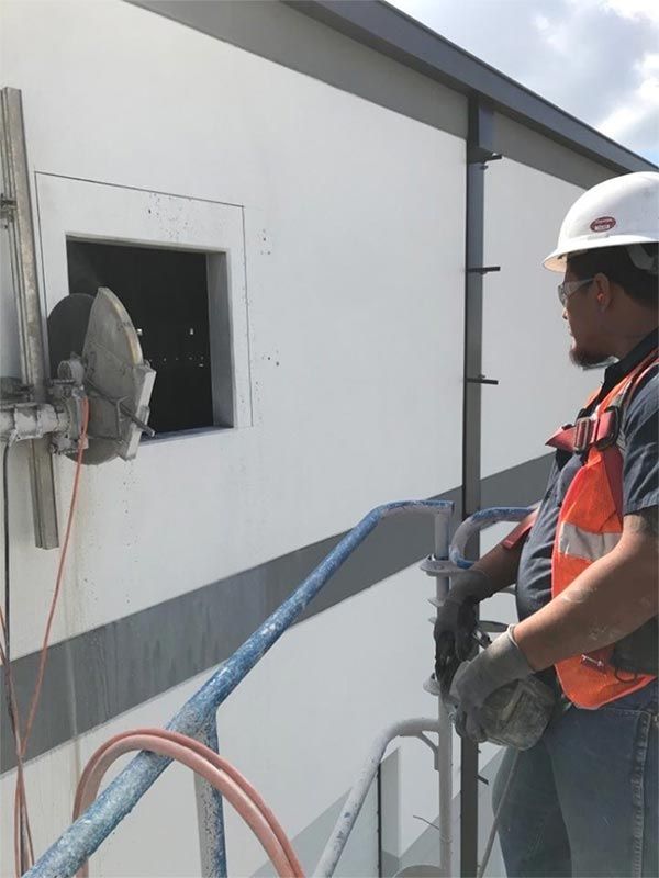 Worker in orange vest and hard hat on a scaffold beside a white building wall and window opening