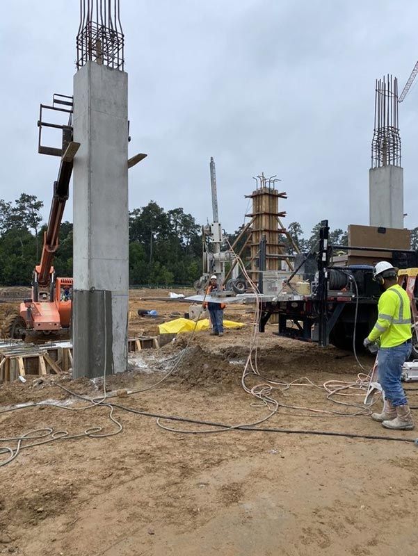 Construction site with concrete pillars, machinery, and workers in a muddy, overcast area