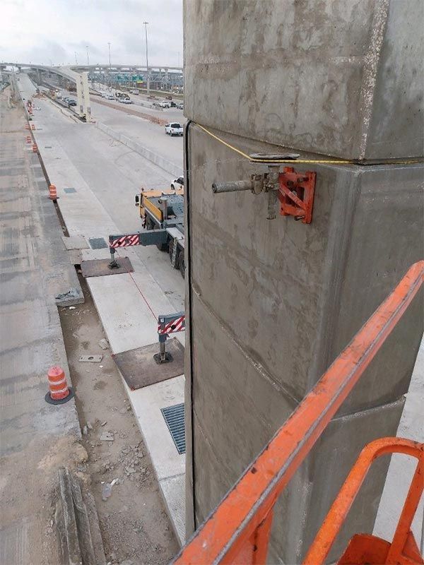 View from a high construction platform overlooking a roadway, with concrete pillars and safety rails.