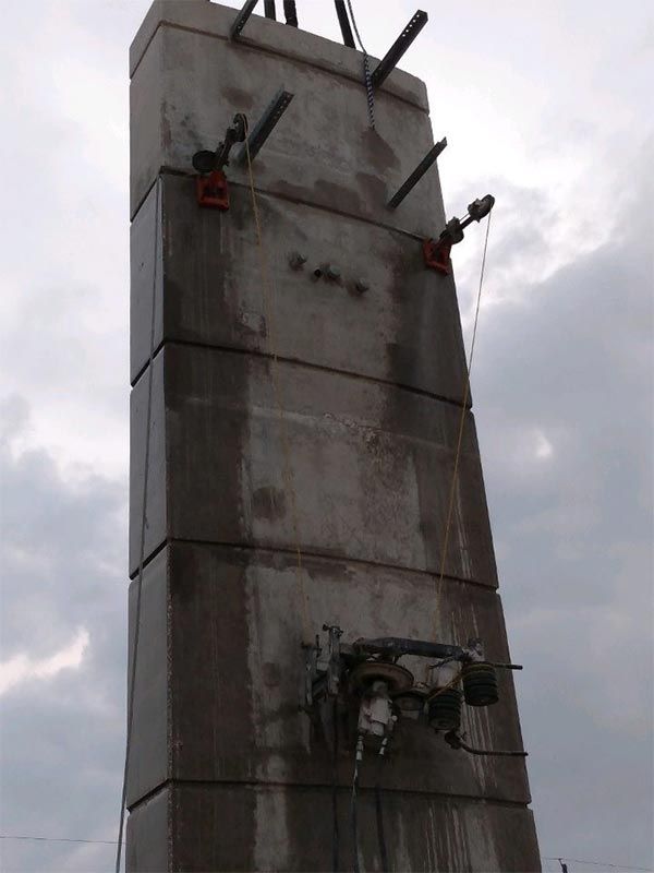 Concrete tower under construction with steel beams protruding against a cloudy sky