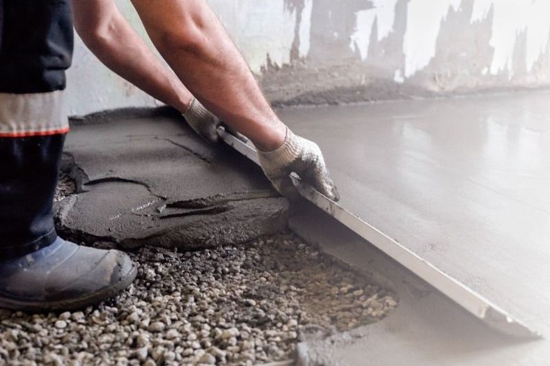Worker smoothing fresh concrete with a trowel on a floor surface