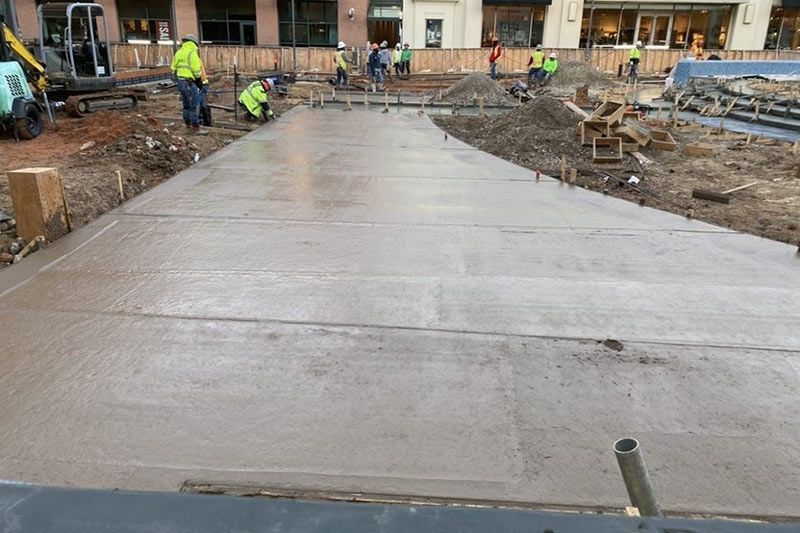 Concrete slab being finished at a construction site with workers in high-visibility gear.