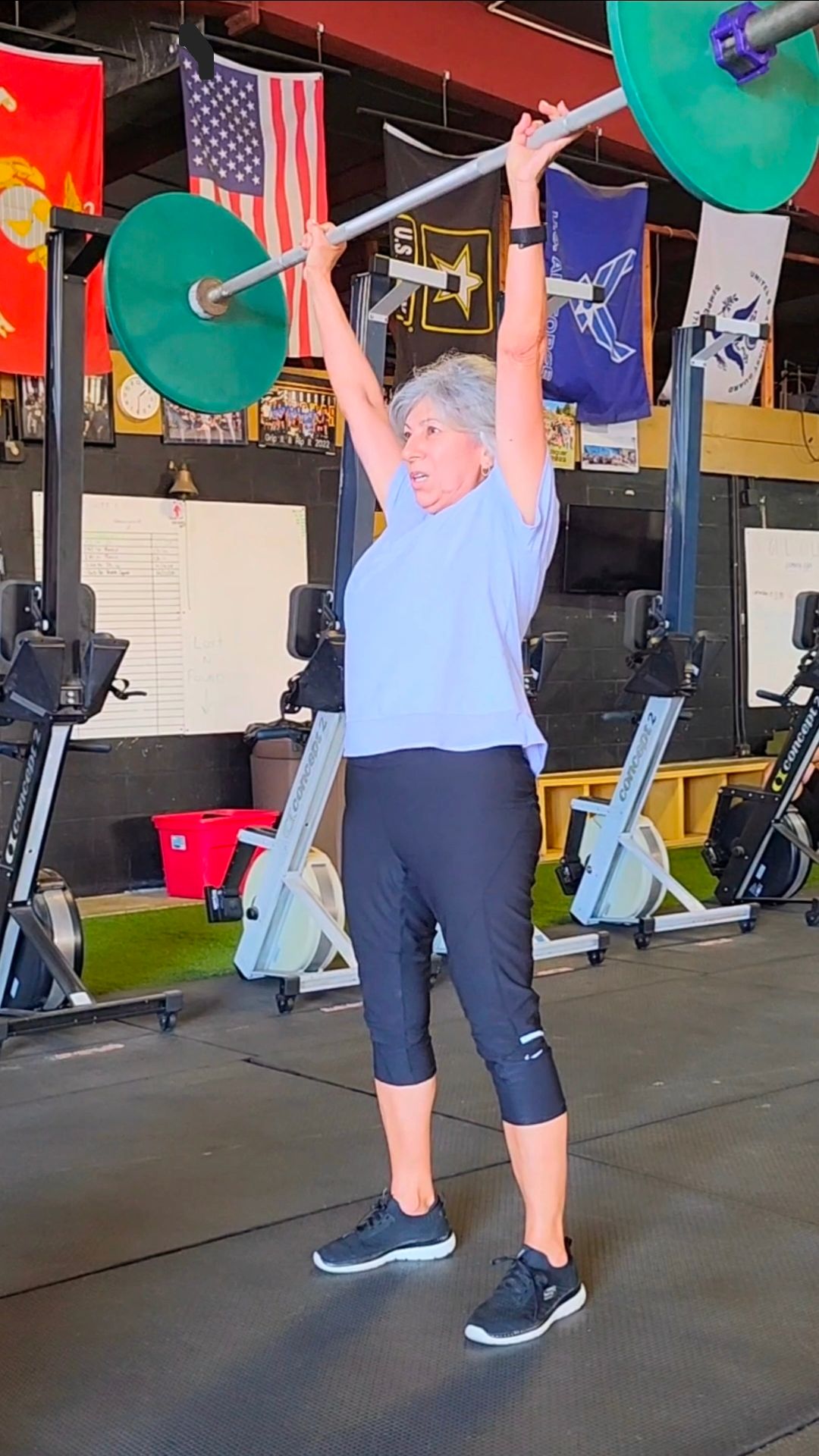 Athlete lifting a barbell overhead at an outdoor gym event, with spectators in the background