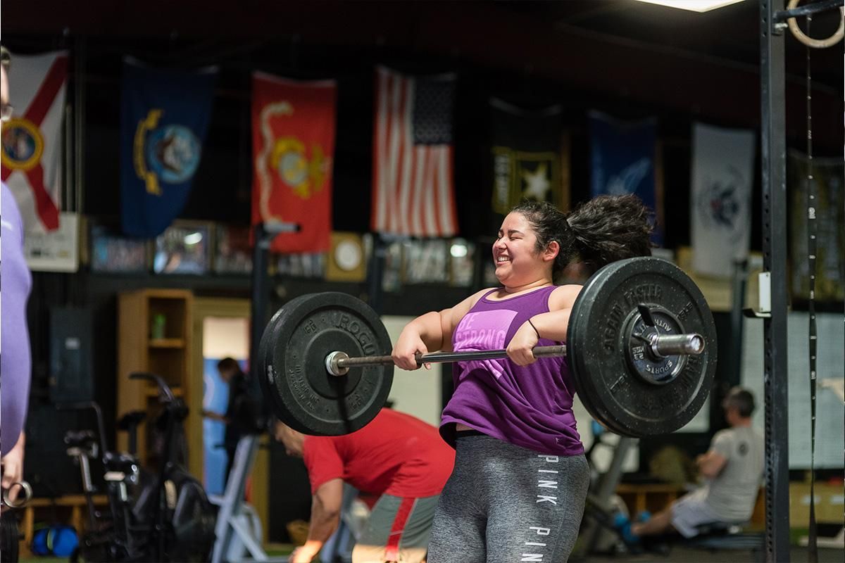 Woman lifting a barbell in CrossFit Jaguar in Tampa,FL, wearing a purple shirt and smiling during a workout.