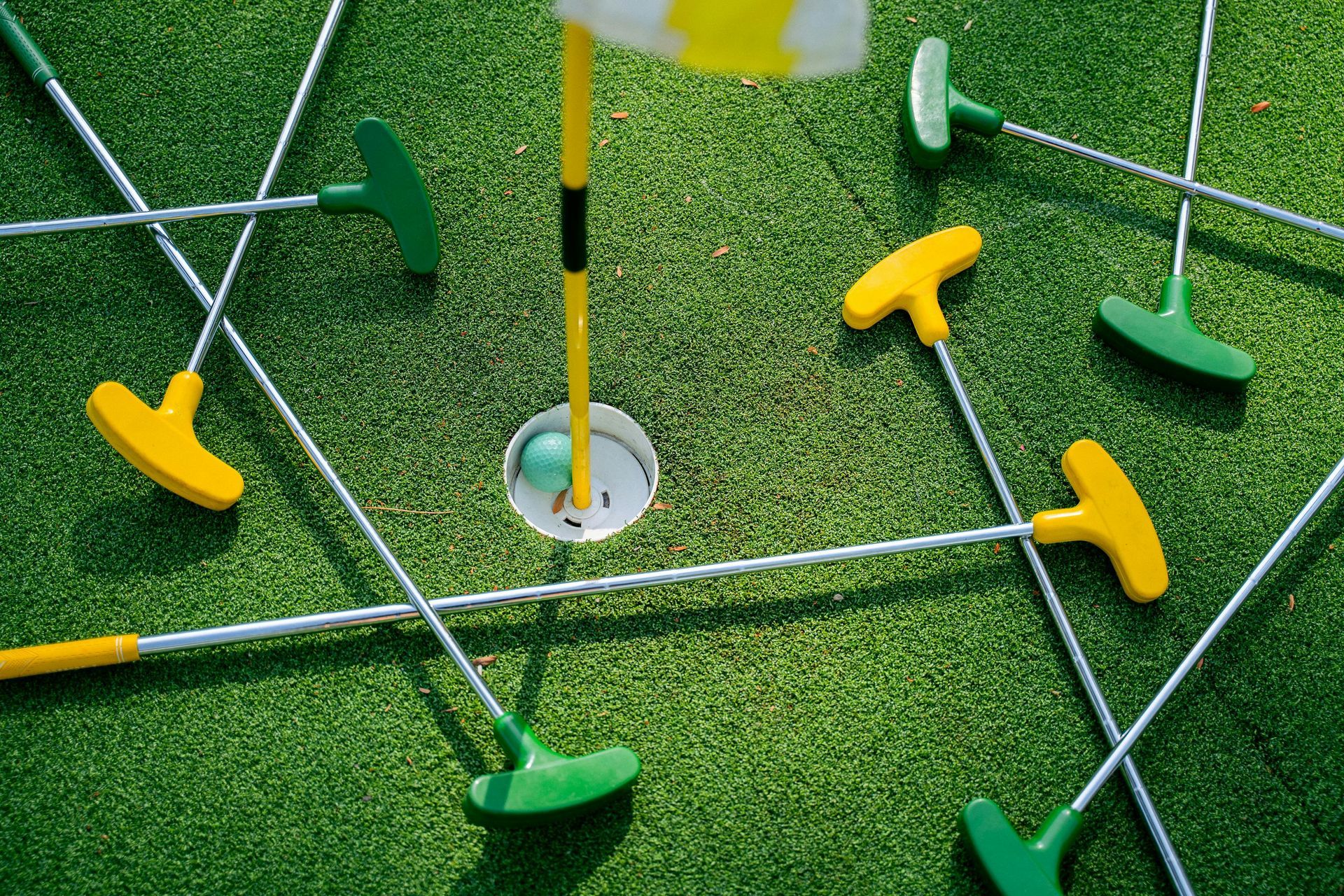 Minigolfloch mit Ball, umgeben von grünen und gelben Puttern.