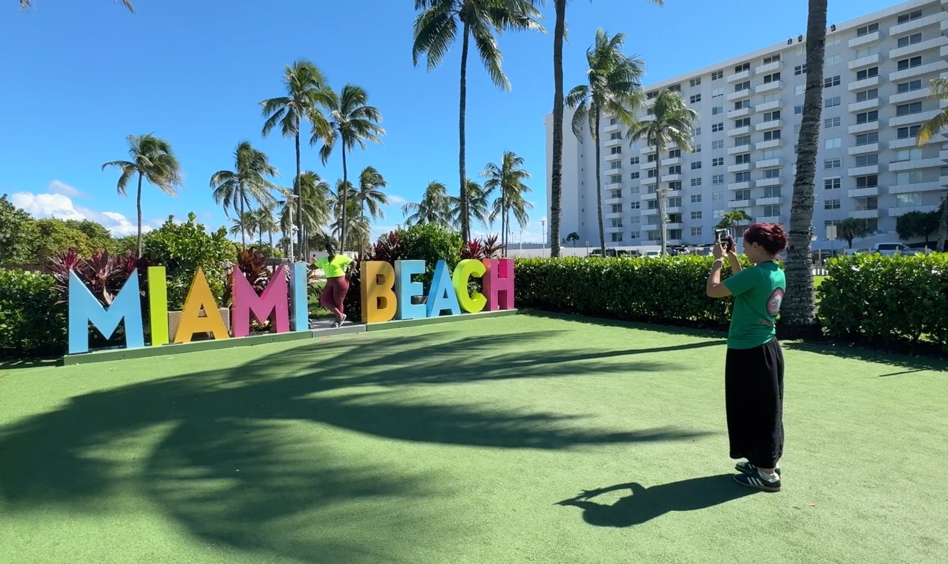 A tour guide helps take photos of a color passenger at the Miami Beach sign.
