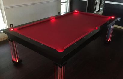 Red-lit pool table in a dark room with a black frame and chrome legs