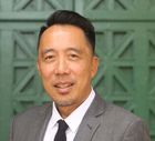 Man in gray suit, smiling, in front of a green, paneled door.