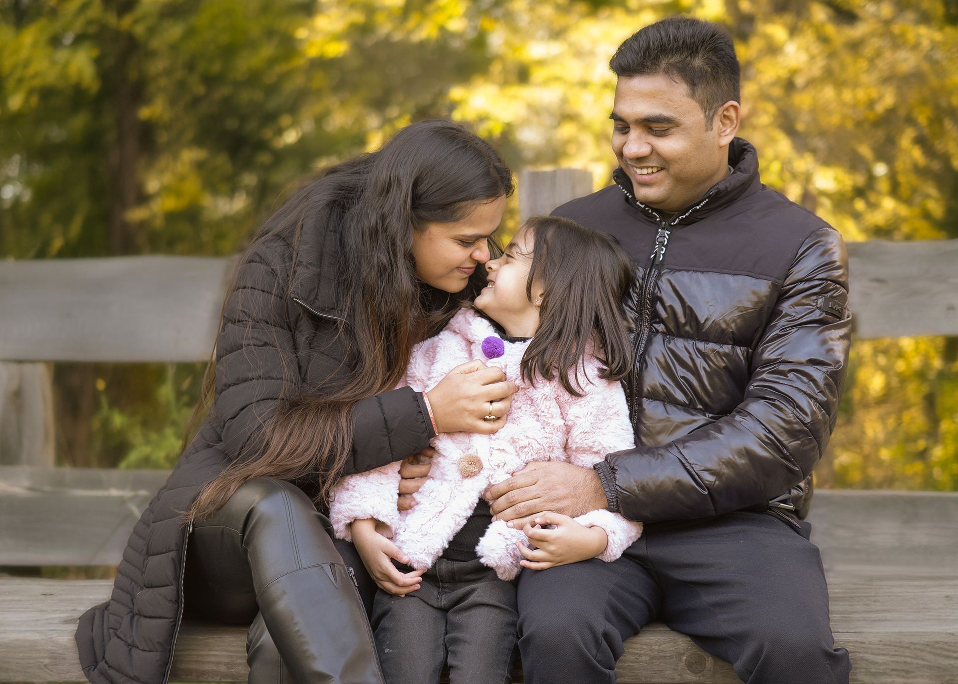 A man and woman are sitting on a bench with a little girl.
